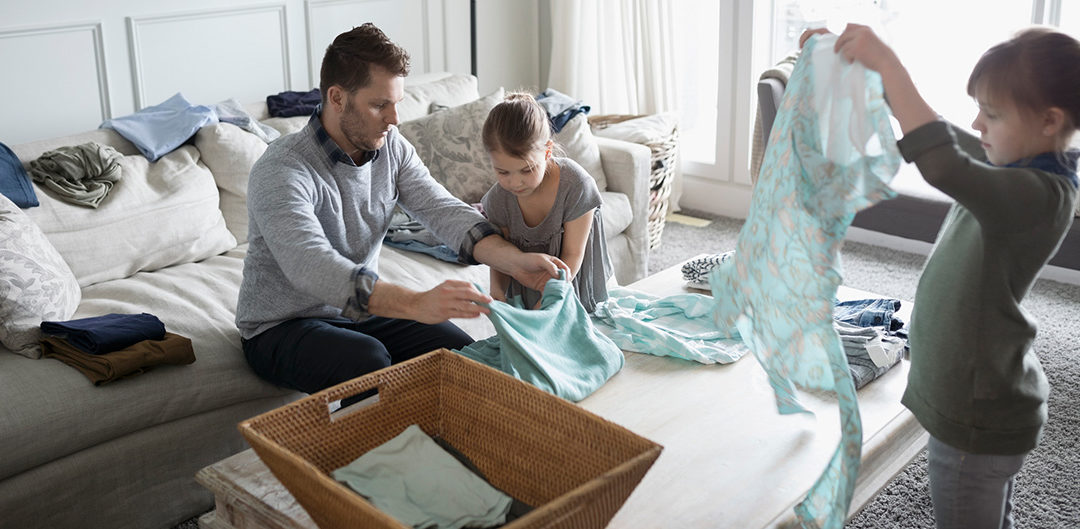 Children helping father fold laundry in living room