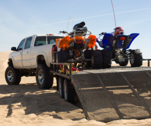two ATVs loaded on the back of a silver truck parked on sand